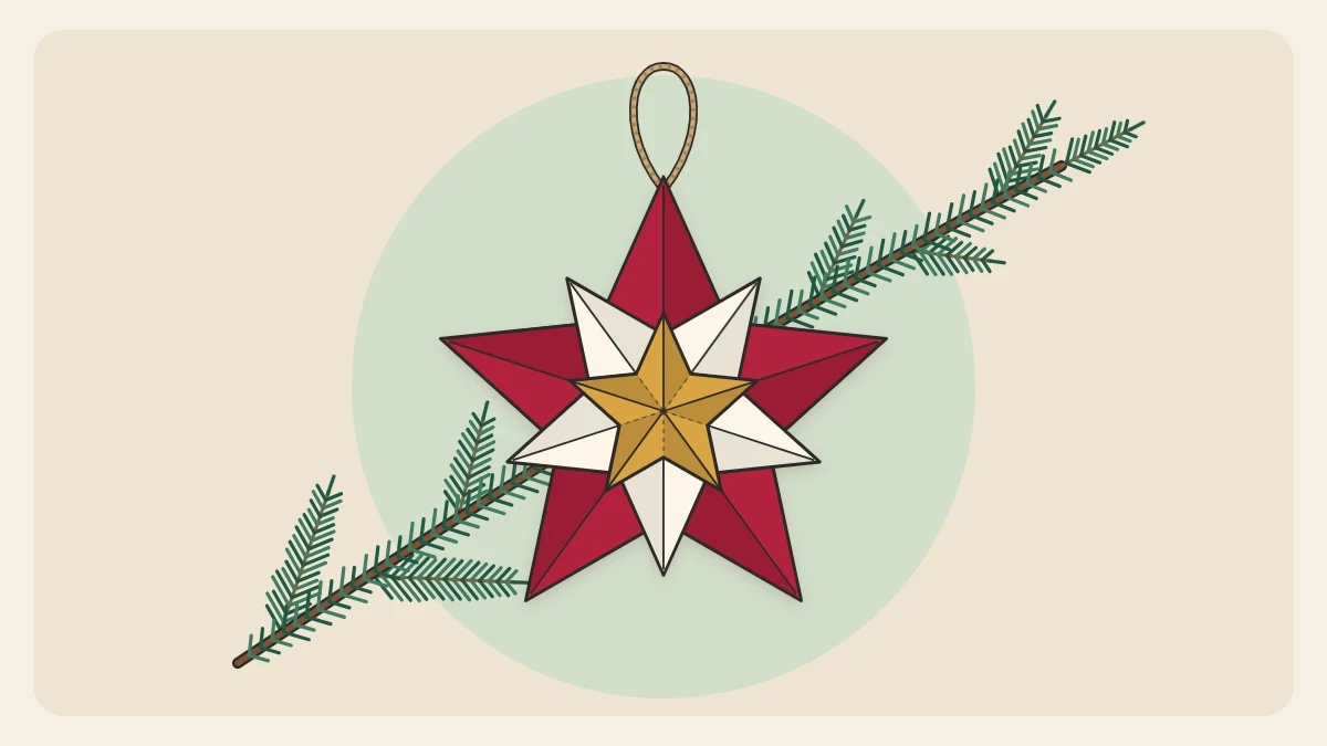 A layered paper star ornament in red, cream and gold tones hanging from a twine loop by an evergreen sprig