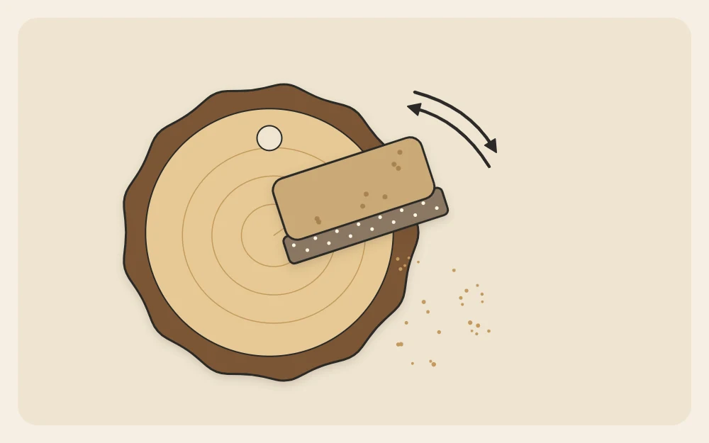 A plain wood slice being sanded with a small sanding block, with a pre-drilled hole near the top edge